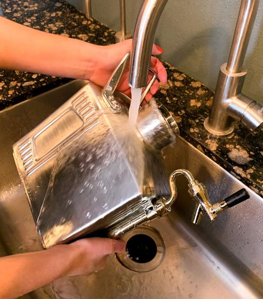 pressurized growler being washed under runing water in a stainless steel sink.