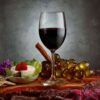 glass of red wine in a 19oz stemmed wine glass on a table with crackers, cheese, and grapes.