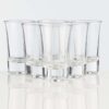 six 1oz shot glasses setup in a v formation on a white background.