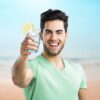 smiling man holding a 13oz italian style blue glass with water and a lemon on the rim.