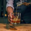 scotch being elegantly poured into a gold embossed buck 13.75 oz whiskey glass