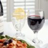 a 10.5 ounce stemmed wine glass half full of red wine next to another smaller glass of water with a lemon.