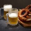 2 beer mugs next to a large soft pretzel.