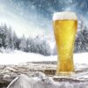 22 ounce wheat beer glass with a pilsner draft in it on a snow laden background.