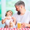 father and daughter, each with their own 22oz glass stein, one filled with milk the other with beer.