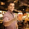 young man holding a full 16oz glass beer mug.