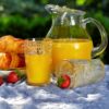 12.75 oz iced tea glass with gold rim and floral cut glass design next to a carafe of orange juice with one glass filled.