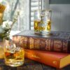 2 pours of whiskey set on a desktop with books in 11.75 ounce double old fashioned whiskey glasses with gold rims.