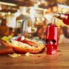 a red skull tiki glass next to a sausage and fries lunch basket.