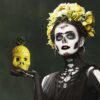 day of dead woman holding a yellow pineapple skull tiki glass in her hand.