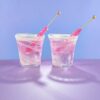 2 pink hard candies in 2 10oz white swirl hand blown rocks glasses on a white counter with blue background.